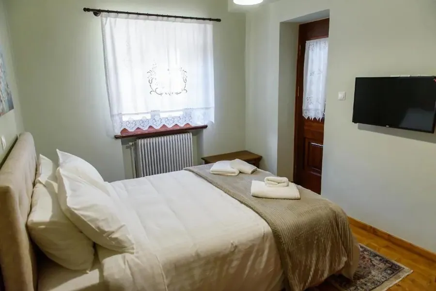 Διπλό κρεβάτι με λευκά σεντόνια δίπλα στο παράθυρο