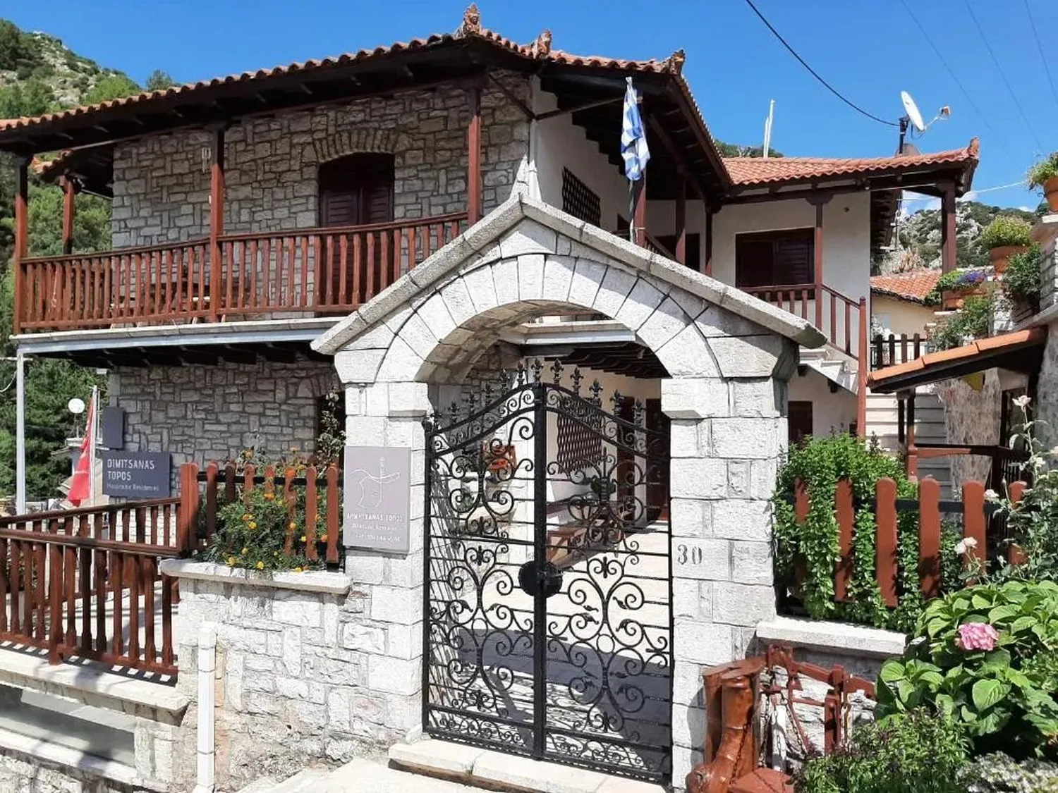 Η πέτρινη καμάρα με τη σιδερένια πόρτα μπροστά στο σπίτι με τα ξύλινα μπαλκόνια