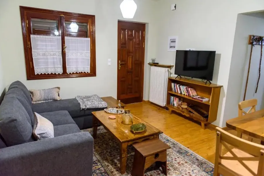 Σαλόνι με γκρι γωνιακό καναπέ, τηλεόραση και ξύλινο παράθυρο